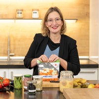 Yvonne Willicks steht in einer Küche und lächelt in die Kamera. In ihrern Händen hält sie einen Gefrierbeutel.