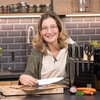 Yvonne Willicks sthet in einer modernen Küche und hält ein scharfes Messer in der Hand. 