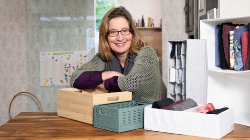 Yvonne Willickst sitzt an einem Thresen. Vor ihr stehen mehrere Organisationssysteme für den Schrank.