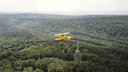 Ein gelber Doppeldecker fliegt über den Teutoburger Wald am Hermannsdenkmal vorbei