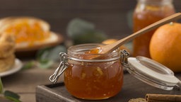Orangenmarmelade in einem kleinen Vorratsglas, mit einem Holzlöffel darin. 