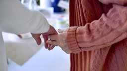 Das Bild zeigt eine Pflegekraft, die die Hand einer Bewohnerin einer Pflegeeinrichtung hält.