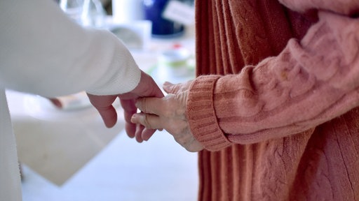 Das Bild zeigt eine Pflegekraft, die die Hand einer Bewohnerin einer Pflegeeinrichtung hält.