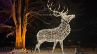 Einw festlich leuchtende Hirschskulptur in einem dünn mit Schnee bedeckten Park.