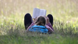 Eine Frau liegt auf einer Wiese und liest in einem Buch. 