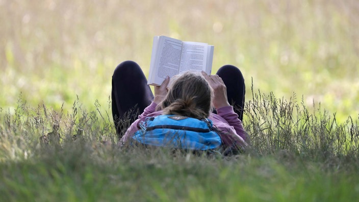 Eine Frau liegt auf einer Wiese und liest in einem Buch. 
