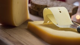 Eine Scheibe mittelalter Gouda wird mit einem Käsehobel vom Stück getrennt.