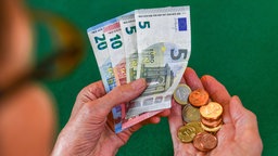 Eine ältere Frau mit Brille hält Euromünzen und -scheine in der Hand.