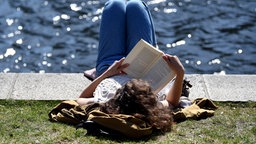 Eine junge Frau ließt ein Buch am Landwehrkanal.