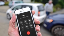 Handy mit gewählter Notrufnummer 110 und einem Autounfall im Hintergrund 