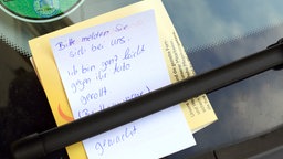 Ein Zettel mit der Aufschrift "Bitte melden Sie sich bei uns. Ich bin ganz leicht gegen Ihr Auto gerollt." am Auto