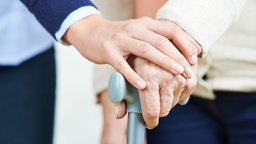 Frau hält die Hand mit einer Seniorin und ihrem Gehstock.