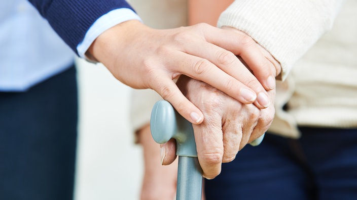 Frau hält die Hand mit einer Seniorin und ihrem Gehstock.