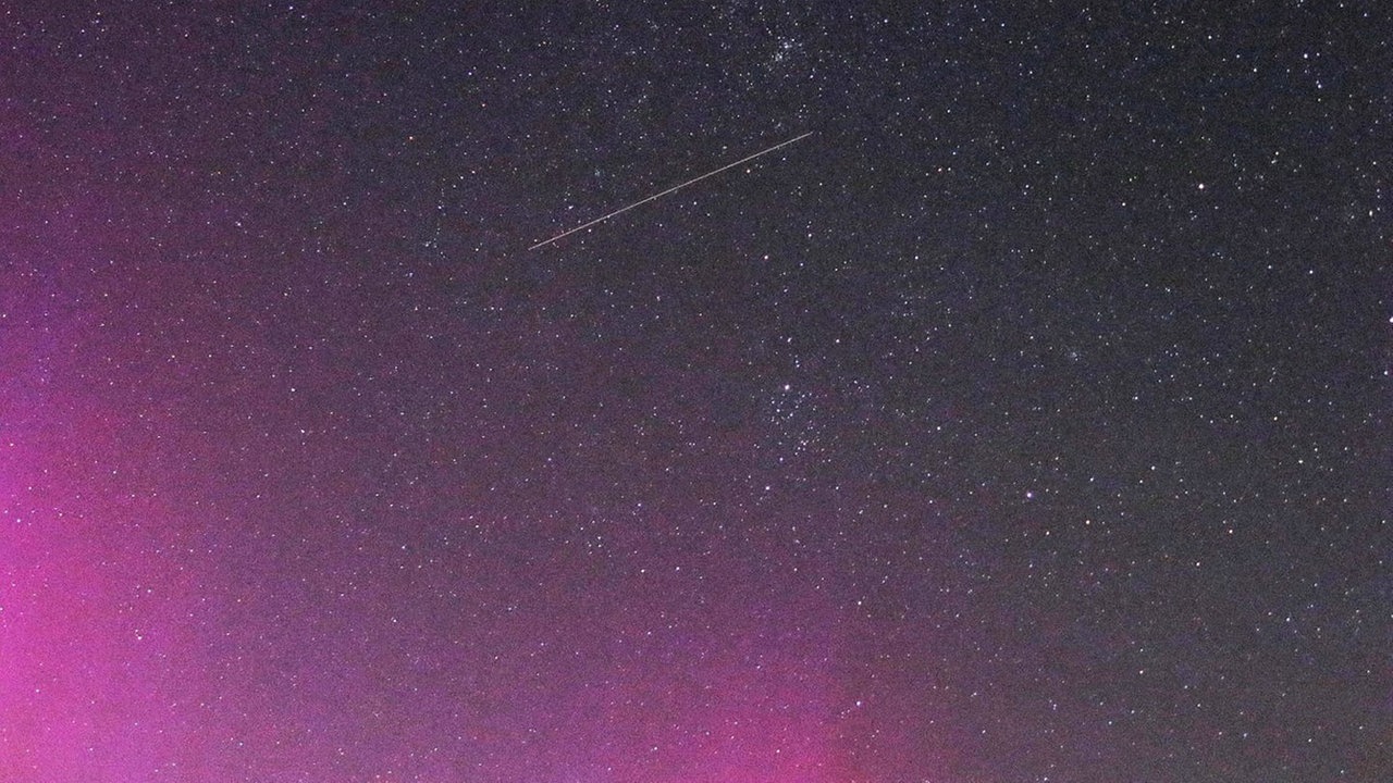 Blick auf den Himmel, dessen Polarlichter eine Sternschnuppe kreuzt.