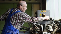 Ein älterer Herr arbeitet in der Werkstatt eines mittelständischen Unternehmens für Maschinenbauteile. 