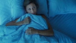 Frau leigt wach im Bett und kann nicht schlafen 