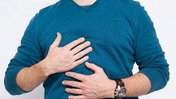 Ein Mann fässt sich vor Schmerzen Bauch und Brust.