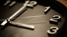 Eine schwarze Wanduhr mit silbernen Zeigern