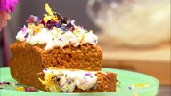 Ein brauner Kuchen verziert mit  kleinen Marzipan-Karotten, in der Mitte ein weißer Klecks, mit einer weiteren kleinen Marzipan-Karotte