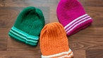 Je eine grüne, rosa- und orangefarbene Strickmütze