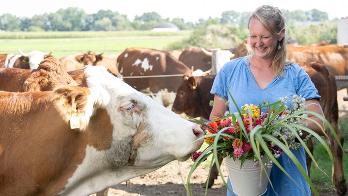 Anna Pröbstle mit Kühen und einem Eimer voller Wildblumen. 
