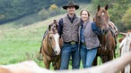 Katharina Deitmers mit ihrem Mann Helge auf der Weide mit Pferden und Longhorn Rindern