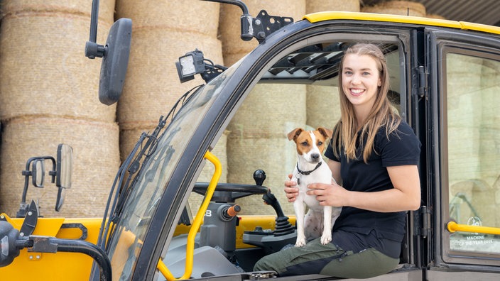 Leonie Froböse sitzt mit Hund Ella auf einem Traktor. 