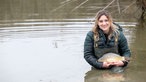 Svenja Viertel steht in einem Fischteich mit einem Karpfen in den Händen. 