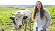 Verena Krimbacher steht auf der Kuhweide, neben ihr eine Kuh.