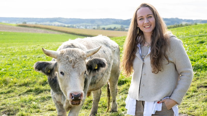 Verena Krimbacher steht auf der Kuhweide, neben ihr eine Kuh.