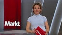 Moderatorin steht vor grauem Hintergrund.