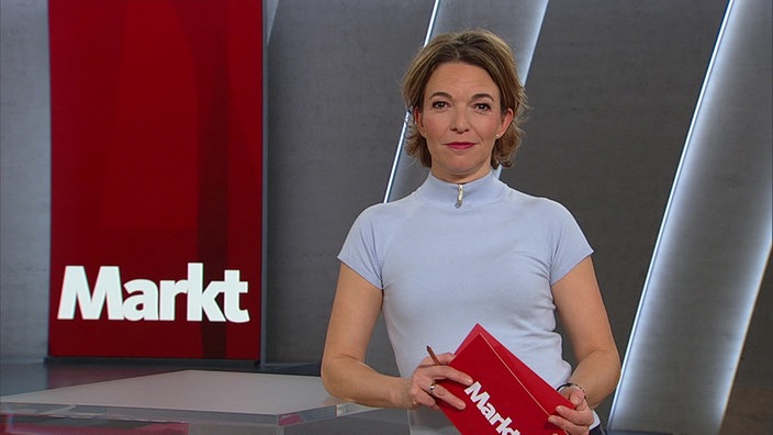 Moderatorin steht vor grauem Hintergrund.