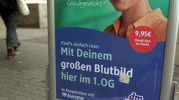 Das Bild zeigt ein Schild des Drogiermarktes "dm" mit der Werbung für eine Blutabnahme.