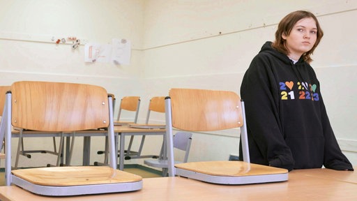 Ein Mädchen steht in einem leerem Klassenraum mit betrübten Blick.