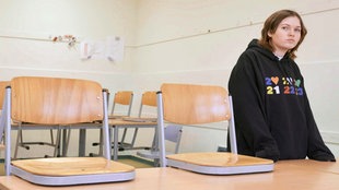 Ein Mädchen steht in einem leerem Klassenraum mit betrübten Blick.