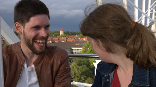 Mann links sitzt mit Frau rechts im Riesenrad. Unter ihnen ist die Stadt Münster zu sehen.