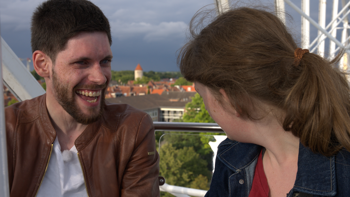 Mann links sitzt mit Frau rechts im Riesenrad. Unter ihnen ist die Stadt Münster zu sehen.
