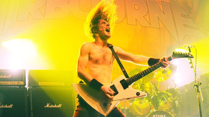 Ein animierter Bassist auf der Bühne, die Haare stehen ihm zu berge