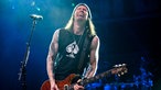 Bandmitglied von Alter Bridge spielt Gitarre und singt dabei mit schmerzverzerrtem Gesicht