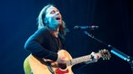 Myles Kennedy sitzt auf einem Hocker und singt mit geschlossenen Augen, während er sich selbst mit der Gitarre begleitet