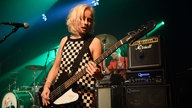 Bassistin von Angelika Express mit ihrem Gibson Thunderbird E-Bass in schwarz mit weißem Schlagbrett, schaut verträumt aufs Griffbrett und spielt einen rockigen Groove mit einem Plektron