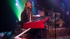 Keyboarder von Big Sugar steht hinter seinen zwei Keyboards, trägt eine lustige Brille und lange Dreads und singt ausgelassen ins Mikrofon