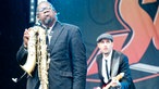 Saxophonist, der sein Instrument falsch herum hält und Bassist, die zusammen zu den anderen Musikern schauen