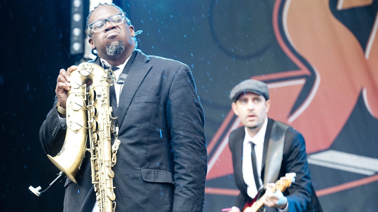 Saxophonist, der sein Instrument falsch herum hält und Bassist, die zusammen zu den anderen Musikern schauen