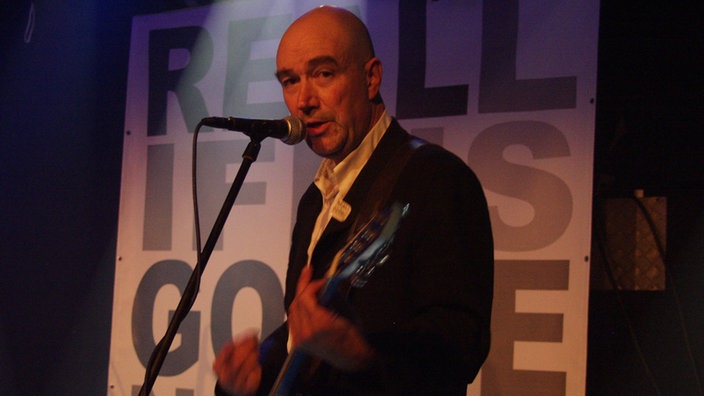 John Watts singt mit Gitarre bei Bootleg im Oktober 2005