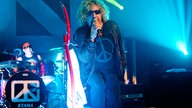 Sammy Hagar, der Sänger der Chickenfoots hält sich mit der rechten Hand das Mikrofon an den Mund. Mit dem rechten Bein stützt er sich ab und lehnt sich zum Publikum nach vorne