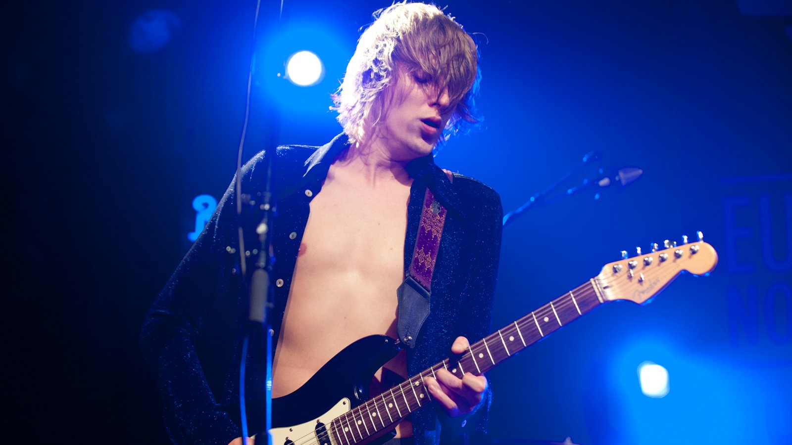 Frontmann Kevin Stunnenberg in echter Rockstar-Pose: verteift im Gitarrenspiel, den Blick gesenkt, das glitzernde Hemd trägt er inzwischen offen, darunter der nackte Oberkörper.