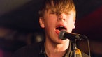 Aufnahme von jungem Kerl mit Pony im Gesicht und offenem Mund beim Singen
