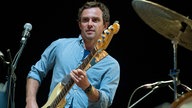 Bassist im hellblauen Hemd zwischen Mirkofon und Schlagzeug