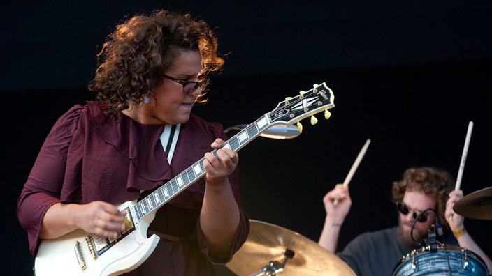 Frontfrau der Alabama Shakes spielt Gitarre und schaut zur Seite, im Hintergrund spielt der Schlagzeuger